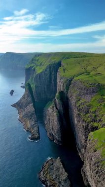 Faroe Adaları 'nın sakin suları üzerinde çarpıcı uçurumlar kulesi. Bereketli yeşil manzara engebeli kıyı şeridiyle çok güzel tezat oluşturuyor., 