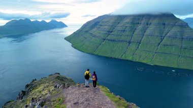Faroe Adaları 'nın göz kamaştırıcı manzarasına bakan iki maceraperest gezgin uçurumun kenarında duruyor. Klakkur zirvesinde bir çift kadın ve erkek.