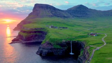 Gasadalur köyü yakınlarındaki okyanusa dökülen Mullafossur şelalesini aydınlatan çarpıcı günbatımına tanık olun. Bereketli yeşil tepeler ve sakin sular büyüleyici bir doğal başyapıt yaratır..