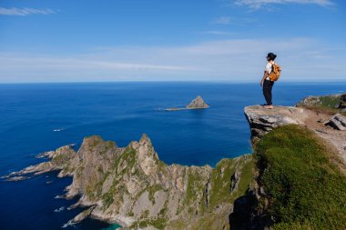 Matind Dağı 'nın kıyısında bir yürüyüşçü, açık güneşli bir günde Andoya, Bleik' i çevreleyen kayalık kıyı şeridinin ve derin mavi okyanusun nefes kesici manzarasının tadını çıkarıyor..