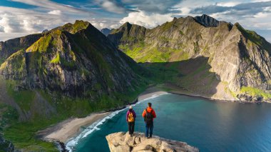 Yürüyüşçüler Ryten Dağı 'nın zirvesinden nefes kesici manzaraya hayran kaldılar. Yeşillik ve engebeli kayalıklar manzaralı Kvalvika Sahili 'ni çevreleyecek. Dalgalar yavaşça kıyıya vuracak..