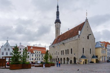 Tallinn, Estonya, 26 Ağustos 2025. Ziyaretçiler, kasvetli ve bulutlu gökyüzünün altında büyüleyici ortaçağ mimarisi ile çevrili büyüleyici kasaba meydanında geziniyor..