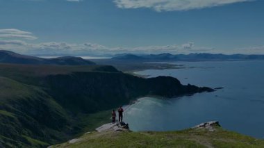 Norveç 'teki Matind Andoy' un çarpıcı kıyı manzarasını keşfedin, açık bir günde deniz ve dağların panoramik manzarasını seyreden dramatik uçurumlar ve yürüyüşçülerin yer aldığı.