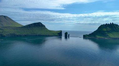 Faroe Adaları 'ndaki sakin suların üzerinde nefes kesen uçurumlar doğal güzellikleri gözler önüne seriyor. Güneş ışığı su yüzeyinde dans eder, engebeli araziyi ve sakin çevreyi vurgular..