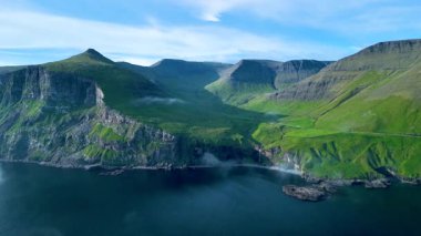 Faroe Adaları 'nın nefes kesici manzarasını keşfetmek, kuş bakışı bir tepeden gökyüzüne çıkmak. Parlak yeşil tepeler huzurlu mavi sularla buluşup sakin bir kaçış yaratıyor..