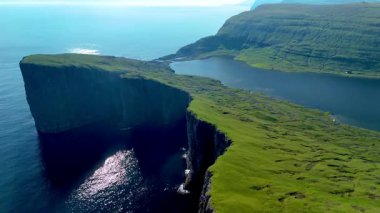 Faroe Adaları 'nın göz kamaştırıcı kayalıkları ve yemyeşil yeşilliği bu hava manzarasında. Sakin sular, güneş batarken canlı manzarayı yansıtıyor ve büyülü bir atmosfer yaratıyor. Sorvagsvatn Gölü, Vagar