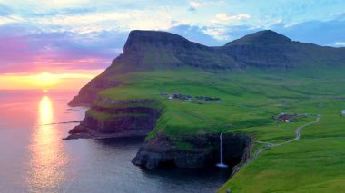 Altın renkler dramatik uçurumları aydınlatırken Mullafossur Şelalesi Gasadalur yakınlarındaki okyanusa dökülüyor. Büyüleyici bir günbatımında Faroe Adaları 'nın dingin güzelliğinin tadını çıkar..