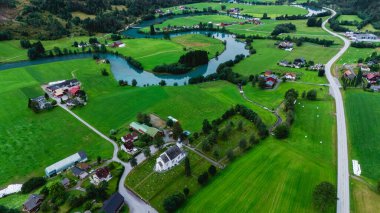 Stryn, Norveç 'in göz kamaştırıcı güzelliğini canlı yeşil tarlaları, dolambaçlı nehirleri ve büyüleyici evleriyle keşfedin. Bu manzara, Norveç kırsalının huzur dolu özünü yansıtıyor..