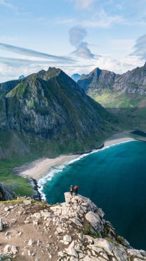 Yürüyüşçüler Norveç 'in Lofoten kentindeki Ryten Kvalvika Beach Trail' deki çarpıcı manzaranın tadını çıkarıyorlar. Engebeli dağlar turkuaz sularla buluşur ve macera için büyüleyici bir zemin oluşturur..