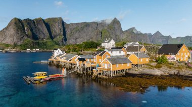 Canlı turuncu renkli balıkçı kulübeleri Sakrisoy 'un rıhtımında gururla durur. Etrafı çarpıcı dağ zirveleriyle çevrilidir..