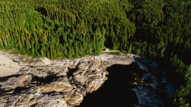Yukardan, canlı yeşilliklerle kusursuz bir şekilde harmanlanmış kayalık kıyılara sahip verimli bir Norveç ormanının sakinliğini hissedin. Doğa aşıkları ve doğa tutkunları için ideal..