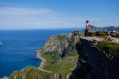 Fiyortların üzerinde yükselen Matind Dağı, Bleik, Andoya 'daki engebeli kıyı şeridine panoramik bir manzara sunuyor. Yeşillik ve engin okyanusla çevrili, tek başına bir yürüyüşçü kenarda durur..