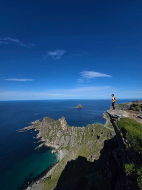 Matind Dağı 'nın kıyısında, Bleik, Andoya' nın çarpıcı sahil kayalıklarına ve masmavi sularına bakan bir gezgin duruyor. Açık mavi gökyüzü huzurlu atmosferi yükseltiyor ve maceraya davetiye çıkarıyor..