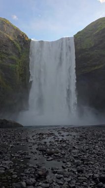 Skogafoss şelalesi zarif bir şekilde kayalıklardan aşağı dökülür. Güneş ışığı suyun üzerinde parıldarken sisli bir manzara yaratır. Ziyaretçiler kayalık kıyı şeridini keşfeder, doğanın nefes kesici güzelliğini yakalar..
