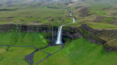 Muhteşem Seljalandsfoss şelalesinin yosunlu uçurumlardan sakin bir vadiye düştüğünü keşfedin..