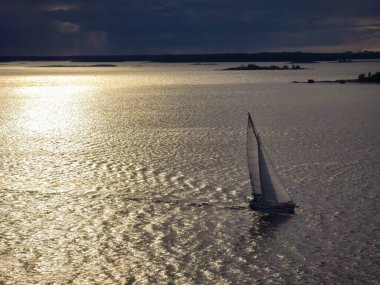 Huzurlu bir sahnede, Finlandiya takımadalarının sakin sularında yüzen bir yelkenli gün batımının ılık parıltısıyla yıkanır. Yumuşak dalgalar yumuşak ışığı yansıtır, barışçıl bir atmosfer yaratır..