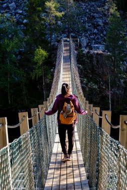 Yürüyüşçünün biri Finlandiya 'nın Hossa Ulusal Parkı' ndaki yemyeşil yemyeşil bir alanda bulunan Julma Olkky Kanyonu üzerinde manzaralı bir asma köprüyü geçer. Huzurlu atmosfer keşif ve macerayı davet eder..