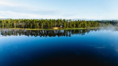 Finlandiya 'da göl kenarında çam ağaçları olan bir karavan. Huzurlu yansımalar, doğa severler ve kaşifler için ideal barışçıl bir atmosfer yaratır..