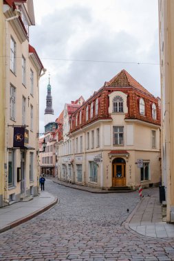 Tallinn, Estonya, 26 Ağustos 2025, antik kaldırım taşı caddesi geleneksel binalarla dolu. Sahne, arka planda bulutlu bir gökyüzünün altında yükselen bir kilise kulesiyle tarihin bir harmanını gösteriyor..