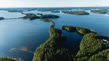 Finlandiya, Punkaharju 'da sakin göller ve yemyeşil ormanlarla çevrili dolambaçlı bir yolu gösteren çarpıcı görüntüyü deneyimleyin. Bu resim sahnesi Fin doğasının özünü yansıtır..
