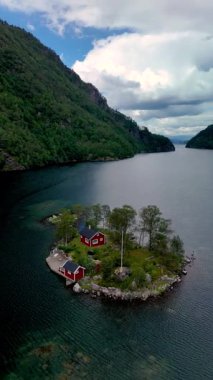 Huzurlu bir fiyortta, Norveç 'te yemyeşil bir adada canlı kırmızı kulübelerden oluşan bir küme duruyor.