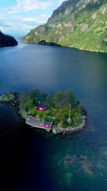 Norveç 'te küçük bir adada bulunan nefes kesici bir tepeden bakıldığında, resim gibi kırmızı bir ev sergileniyor. Bereketli yeşillik kıyı şeridini çevreleyen sakin sular, canlı bir gökyüzünü yansıtıyor..
