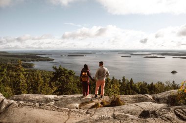 İki yürüyüşçü Koli Milli Parkı 'ndaki kayalık bir çıkıntıda durup göz kamaştırıcı göl manzarasına ve parlak bir gökyüzünün altındaki engin ormanlara bakıyorlar. Doğanın sükuneti onları keşfederken sarar..
