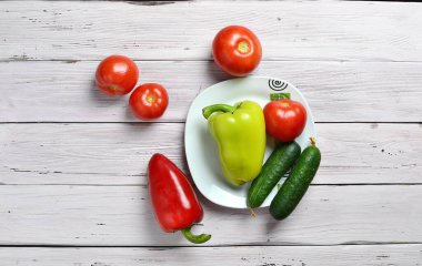 domatesli, salatalıklı, biberli ve tabaklı eski bir ahşap ışıklı sade masa.