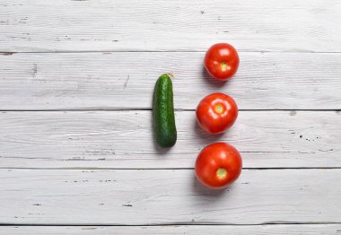 Üç kırmızı domates ve bir yeşil salatalığı eski bir ahşap kırsal masa üzerinde yakın çekim