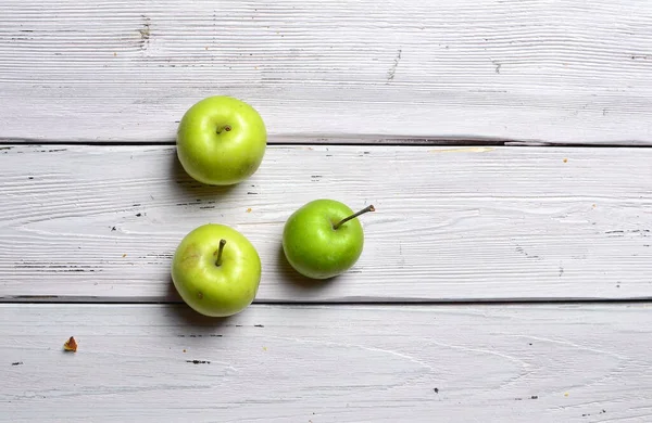 three green apples on white rustic wooden background, top view, copy space
