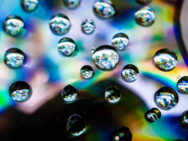 Yağmur suyu damlaları CD 'ye düşüyor ve güneş ışığını yansıtıyor. Sarı mavi ve kırmızı ışık yansıtılıyor.