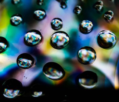 Yağmur suyu damlaları CD 'ye düşüyor ve güneş ışığını yansıtıyor. Sarı mavi ve kırmızı ışık yansıtılıyor.