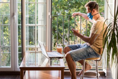 Yüz maskeli bir adam cep telefonuna danışıyor terasın yanında oturuyor.