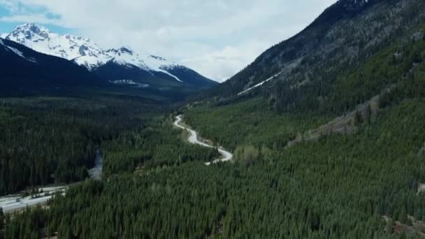 俯瞰环绕着群山的山谷中蜿蜒曲折的道路 多雪的山峰 绿松林覆盖的山丘 — 图库视频影像