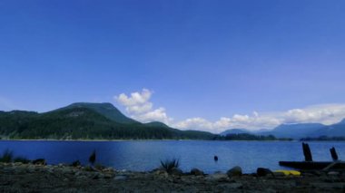 Gölde zaman geçiyor, hareket eden bulutlar ve tepeler ladin ağaçlarıyla kaplı.