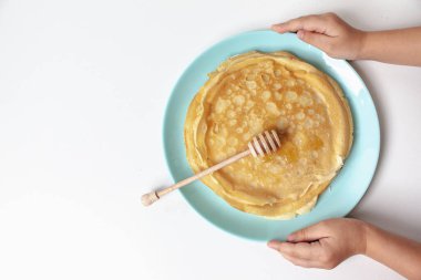 Lezzetli krepler mavi bir tabakta yatıyor. Bir çocuk beyaz bir arka planda ballı krep tabağı tutar..