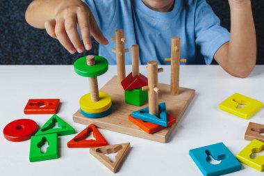 Çocuk Montessori oyunu oynuyor. Çocuk tahta oyuncak ayırıcı topluyor. Çok renkli geometrik şekiller, daire, kare, üçgen, dikdörtgen.
