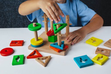 Çocuk Montessori oyunu oynuyor. Çocuk tahta oyuncak ayırıcı topluyor. Çok renkli geometrik şekiller, daire, kare, üçgen, dikdörtgen.