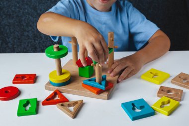 Çocuk Montessori oyunu oynuyor. Çocuk tahta oyuncak ayırıcı topluyor. Çok renkli geometrik şekiller, daire, kare, üçgen, dikdörtgen.