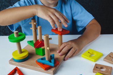 Çocuk Montessori oyunu oynuyor. Çocuk tahta oyuncak ayırıcı topluyor. Çok renkli geometrik şekiller, daire, kare, üçgen, dikdörtgen.