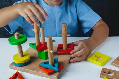 Çocuk Montessori oyunu oynuyor. Çocuk tahta oyuncak ayırıcı topluyor. Çok renkli geometrik şekiller, daire, kare, üçgen, dikdörtgen.