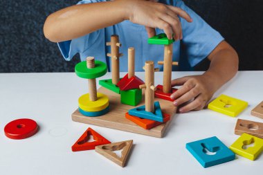 Çocuk Montessori oyunu oynuyor. Çocuk tahta oyuncak ayırıcı topluyor. Çok renkli geometrik şekiller, daire, kare, üçgen, dikdörtgen.