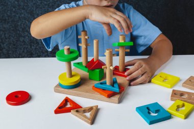 Çocuk Montessori oyunu oynuyor. Çocuk tahta oyuncak ayırıcı topluyor. Çok renkli geometrik şekiller, daire, kare, üçgen, dikdörtgen.