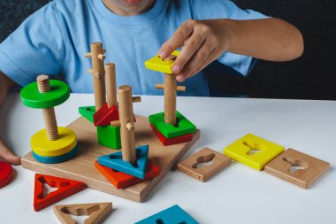 Çocuk Montessori oyunu oynuyor. Çocuk tahta oyuncak ayırıcı topluyor. Çok renkli geometrik şekiller, daire, kare, üçgen, dikdörtgen.