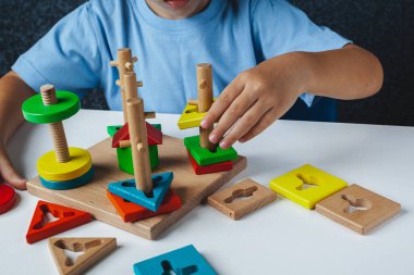 Çocuk Montessori oyunu oynuyor. Çocuk tahta oyuncak ayırıcı topluyor. Çok renkli geometrik şekiller, daire, kare, üçgen, dikdörtgen.