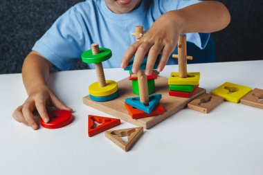 Çocuk Montessori oyunu oynuyor. Çocuk tahta oyuncak ayırıcı topluyor. Çok renkli geometrik şekiller, daire, kare, üçgen, dikdörtgen.