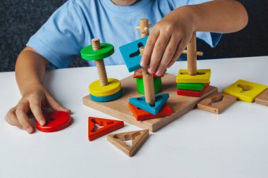 Çocuk Montessori oyunu oynuyor. Çocuk tahta oyuncak ayırıcı topluyor. Çok renkli geometrik şekiller, daire, kare, üçgen, dikdörtgen.