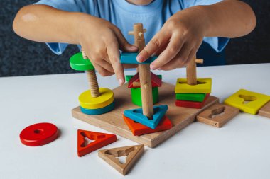 Çocuk Montessori oyunu oynuyor. Çocuk tahta oyuncak ayırıcı topluyor. Çok renkli geometrik şekiller, daire, kare, üçgen, dikdörtgen.
