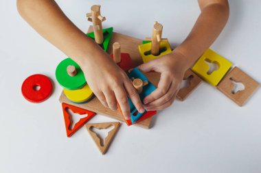 Çocuk Montessori oyuncağı oynuyor. Beyaz arka planda çok renkli mantık sıralayıcısı. Bebek Eller yakın çekim. Tahta geometrik şekiller daire, kare, üçgen, dikdörtgen. Yukarıdan görüntüle