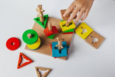 Çocuk Montessori oyuncağı oynuyor. Beyaz arka planda çok renkli mantık sıralayıcısı. Bebek Eller yakın çekim. Tahta geometrik şekiller daire, kare, üçgen, dikdörtgen. Yukarıdan görüntüle